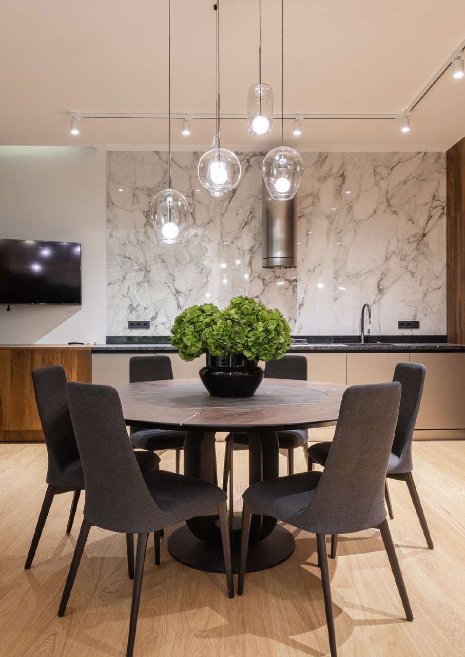 Round dining table under glass pendants beside a marble kitchen wall