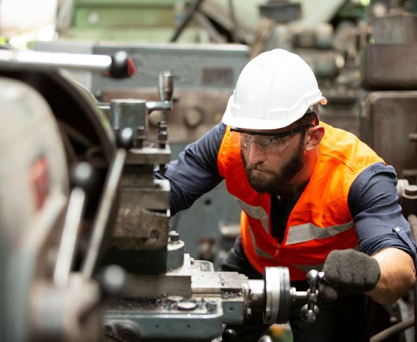 Technician in a hard hat operating a lathe in the workshop